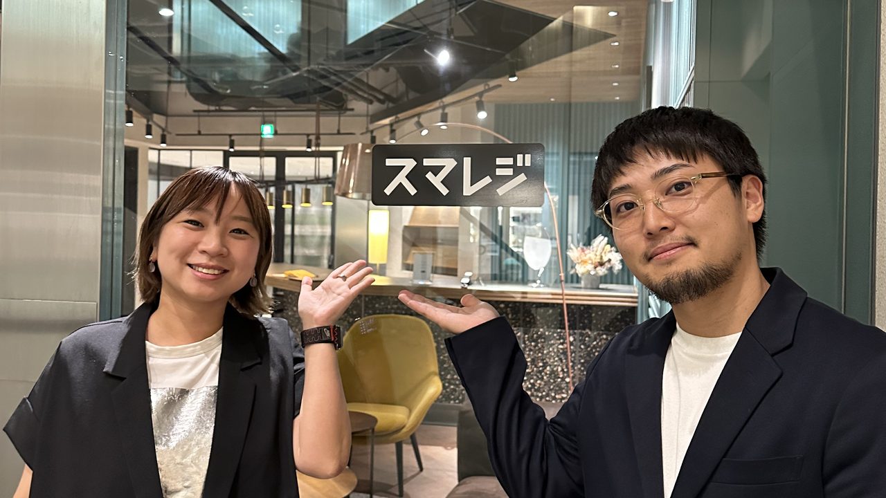 株式会社スマレジのオフィスで、ロゴサインの前に並ぶ2名